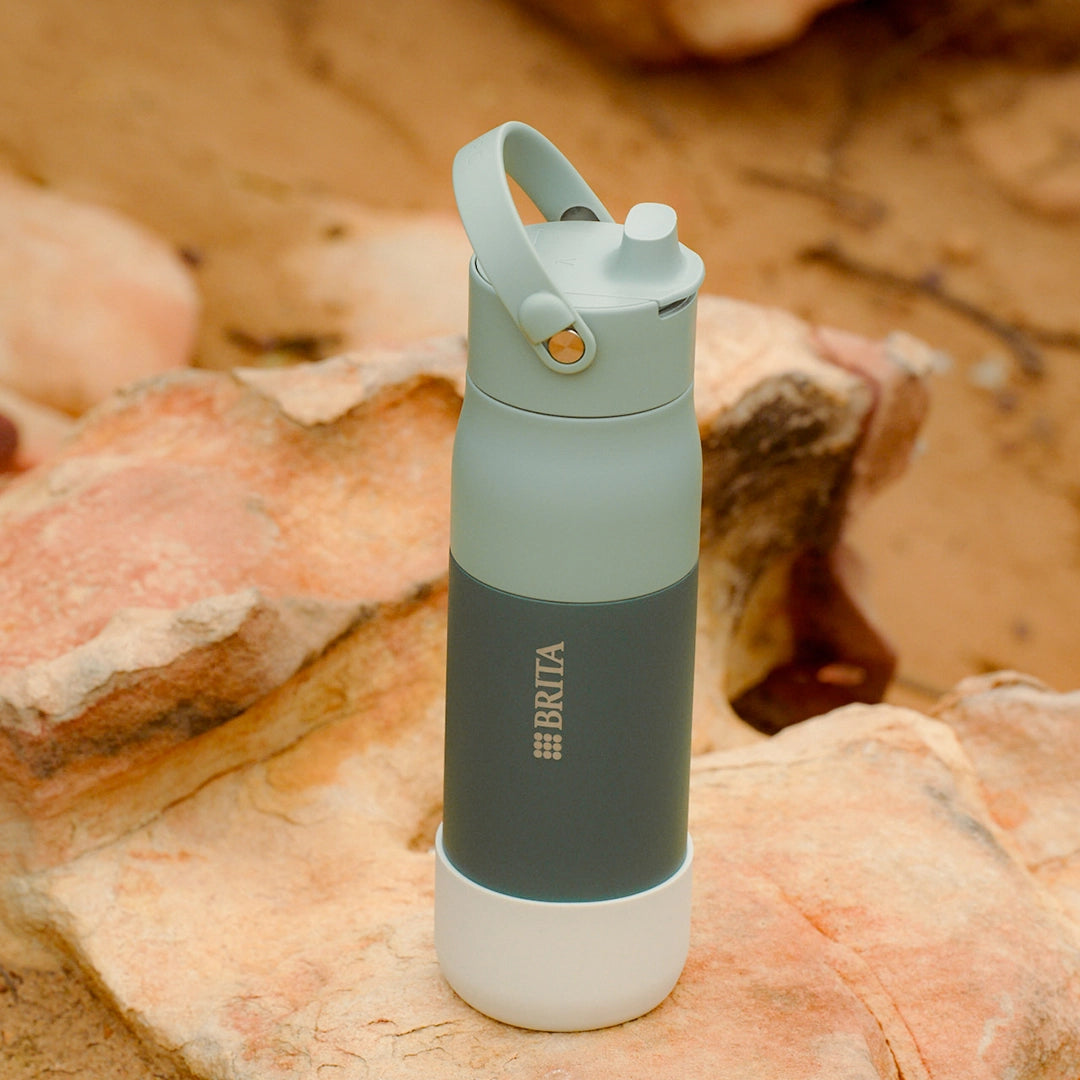 Green BRITA LARQ water bottle with white silicone boot on a stone.