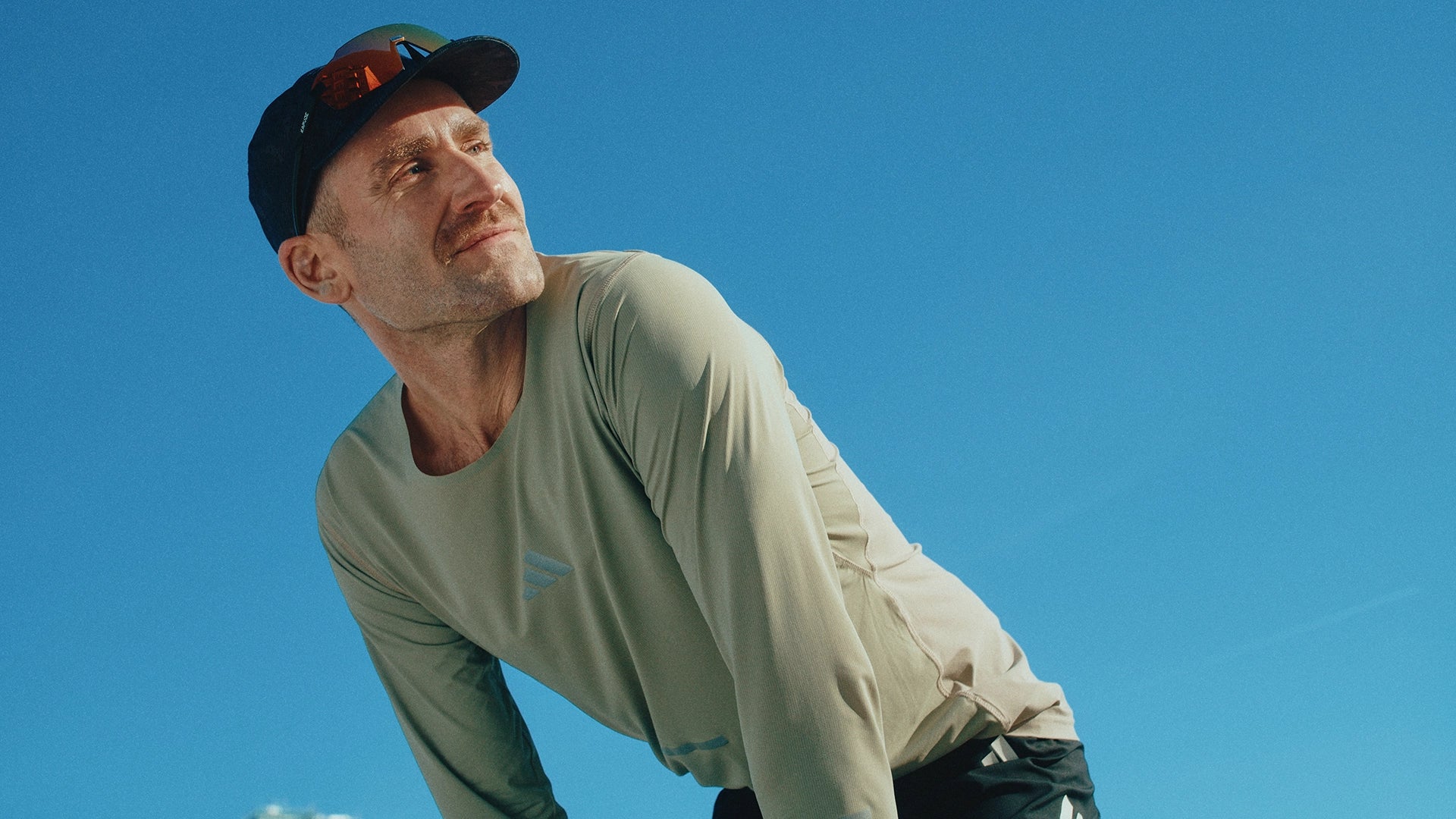 Man in light-colored shirt and cap against a clear blue sky.