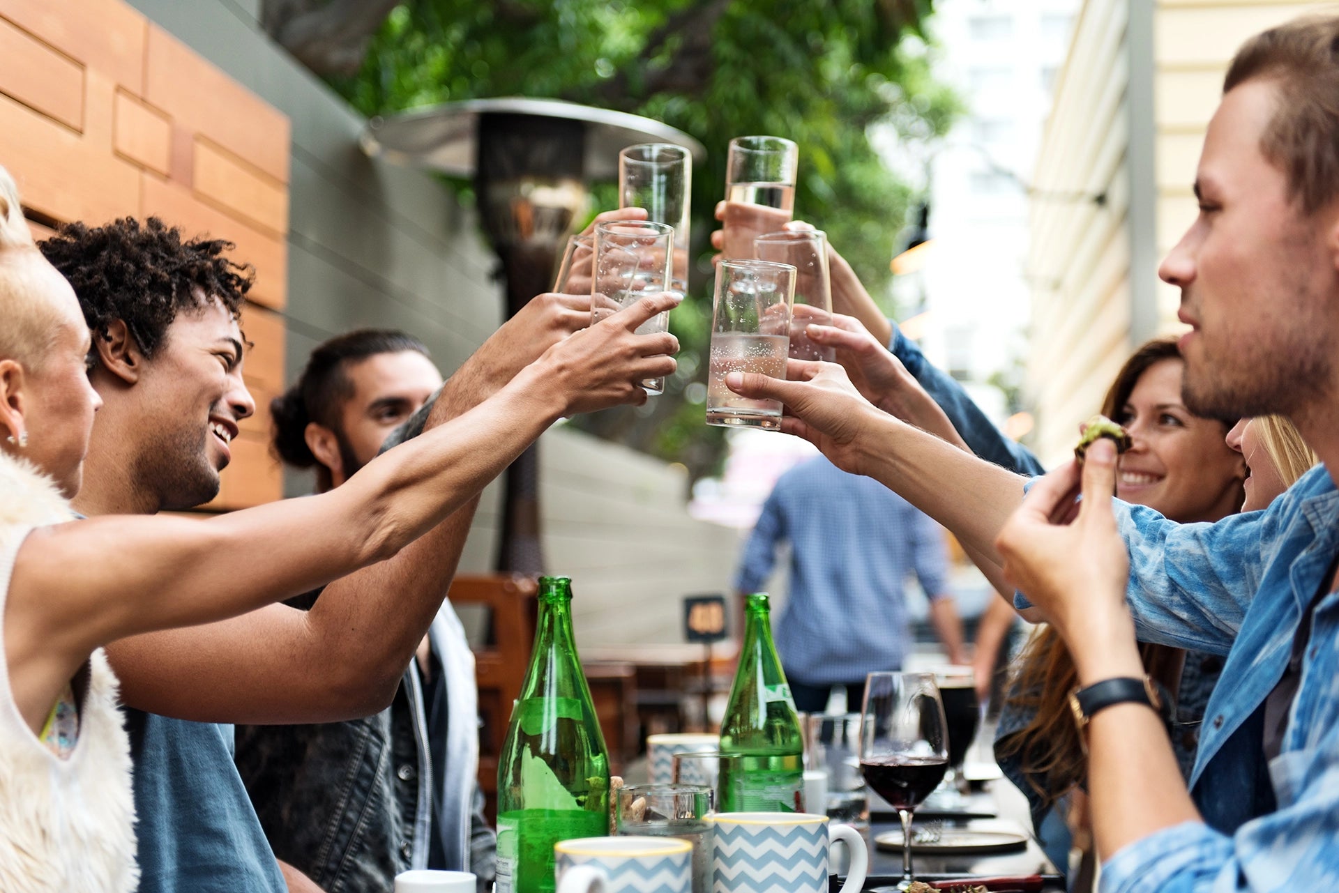A group of friends raising their glasses in a toast at an outdoor patio dining table.