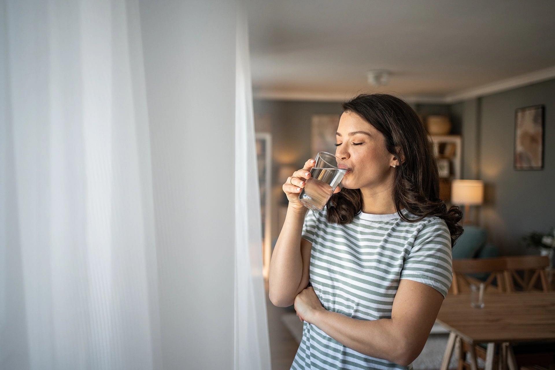 Person drinking a glass of water while standing in a living room