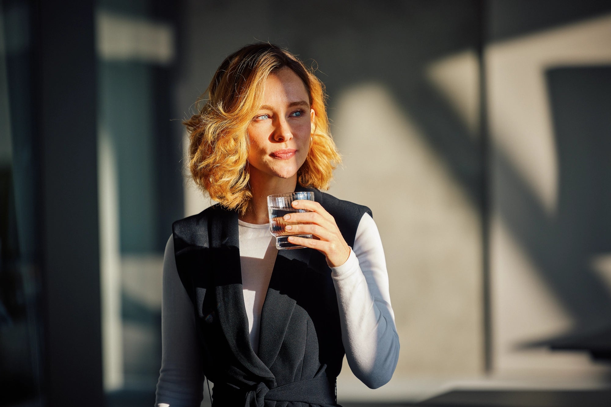 Woman with red hear holding a glass of water in an urban setting