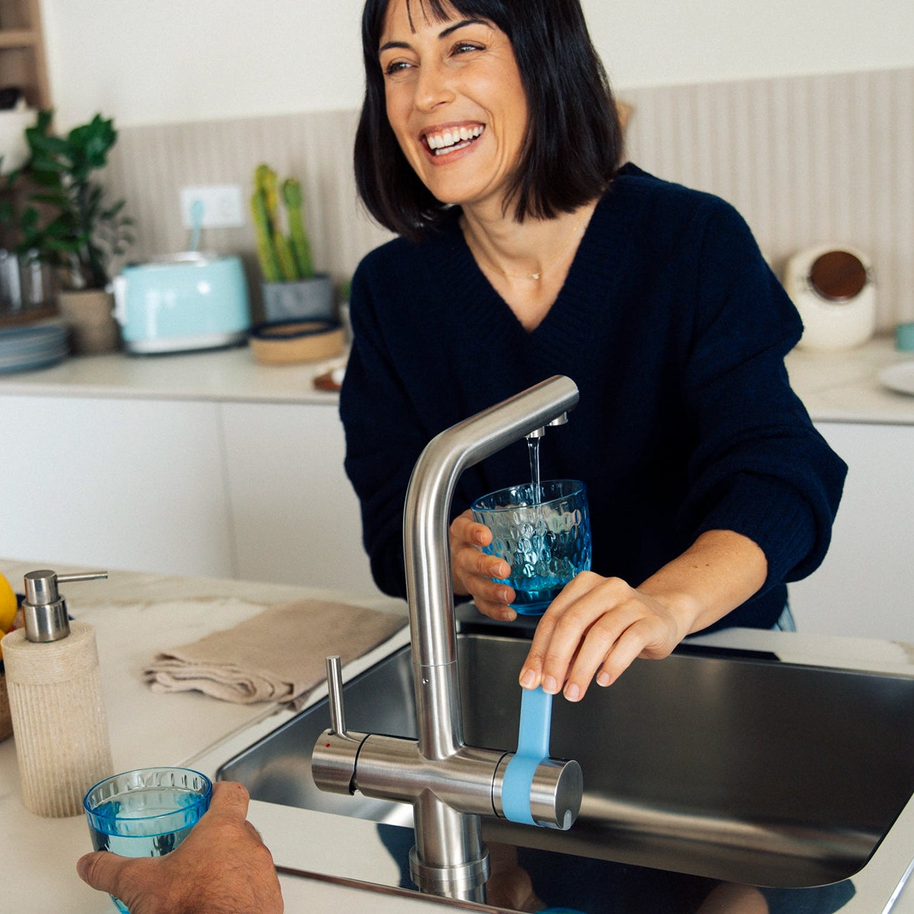 Vrouw die water uit de BRITA 3-way waterkan schenkt filter schenkt ze een glas in in de keuken, terwijl er een man naast haar staat.